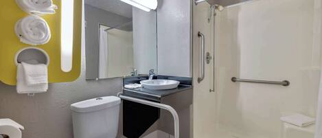 A bathroom with a toilet, sink, and shower. There are towels on the wall and a handrail in the shower.