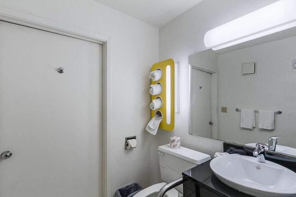 A bathroom with a toilet, sink, mirror, towel rack, and a yellow towel dispenser.