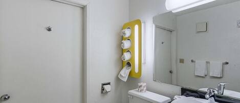 A bathroom with a toilet, sink, mirror, towel rack, and a yellow towel dispenser.