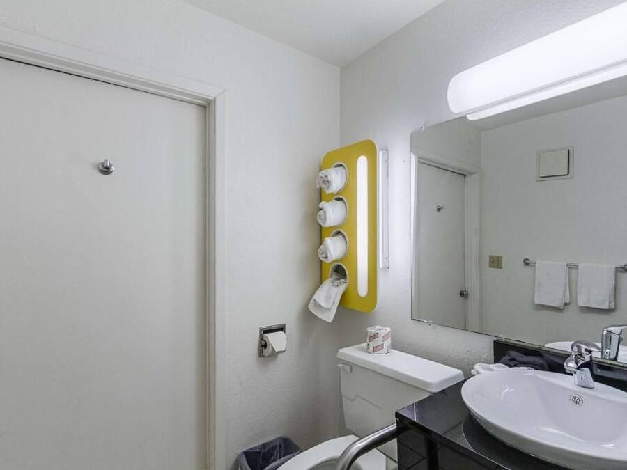 A bathroom with a toilet, sink, mirror, towel rack, and a yellow towel dispenser.