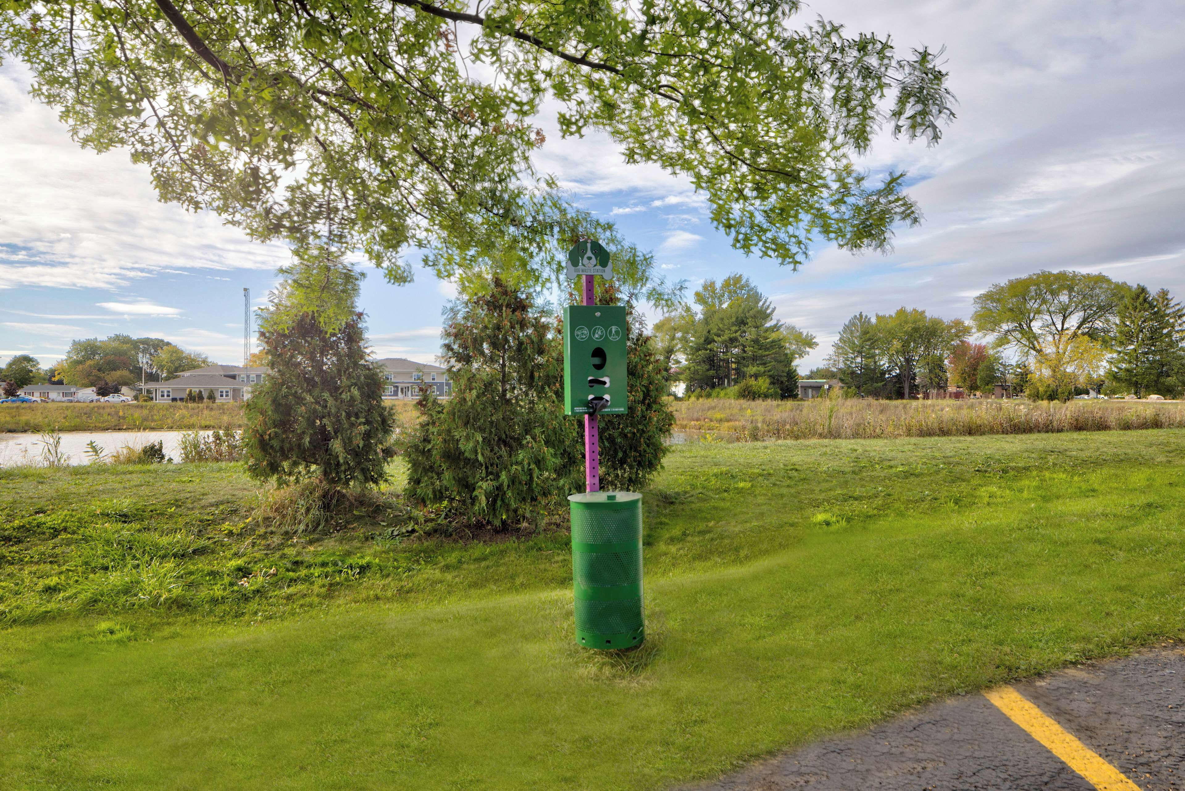 A green roadside sign with a pedestrian crossing symbol, surrounded by grass and trees.