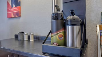 A coffee machine with a colorful design, a stainless steel container, and a metal pitcher on a countertop.