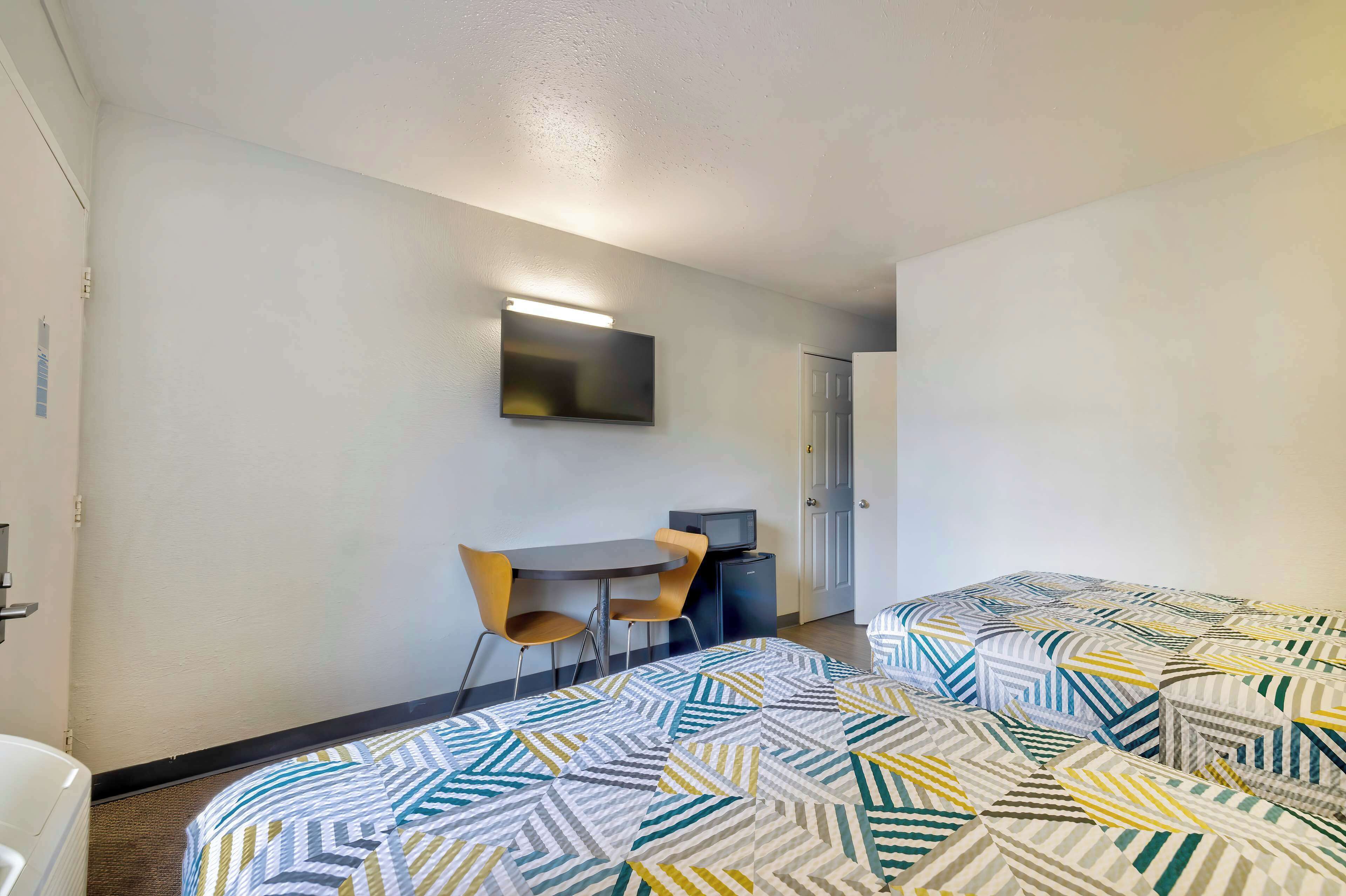 Ein Hotelzimmer mit zwei Betten, einem Schreibtisch mit Stuhl, einem Fernseher und einer Tür.