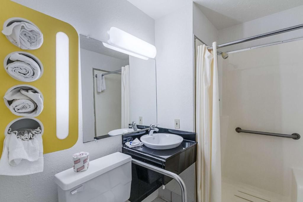 Un baño con lavamanos blanco, espejo, toallero con toallas, inodoro y zona de ducha.