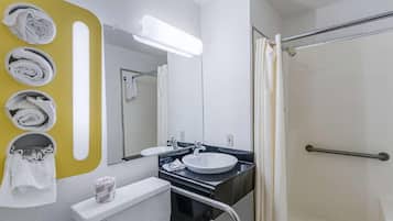 Un baño con lavamanos blanco, espejo, toallero con toallas, inodoro y zona de ducha.
