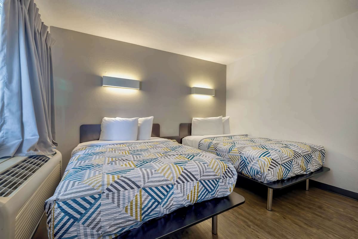 A hotel room with two beds, a heater, and wall-mounted lights.