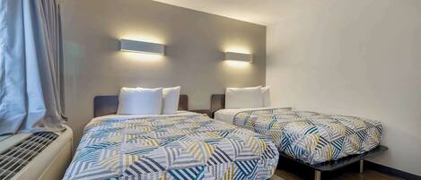 A hotel room with two beds, a heater, and wall-mounted lights.
