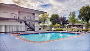 A swimming pool with a blue border, a white building with a balcony, and a fenced area with lounge chairs. - Motel 6 Oshkosh, WI (Oshkosh)