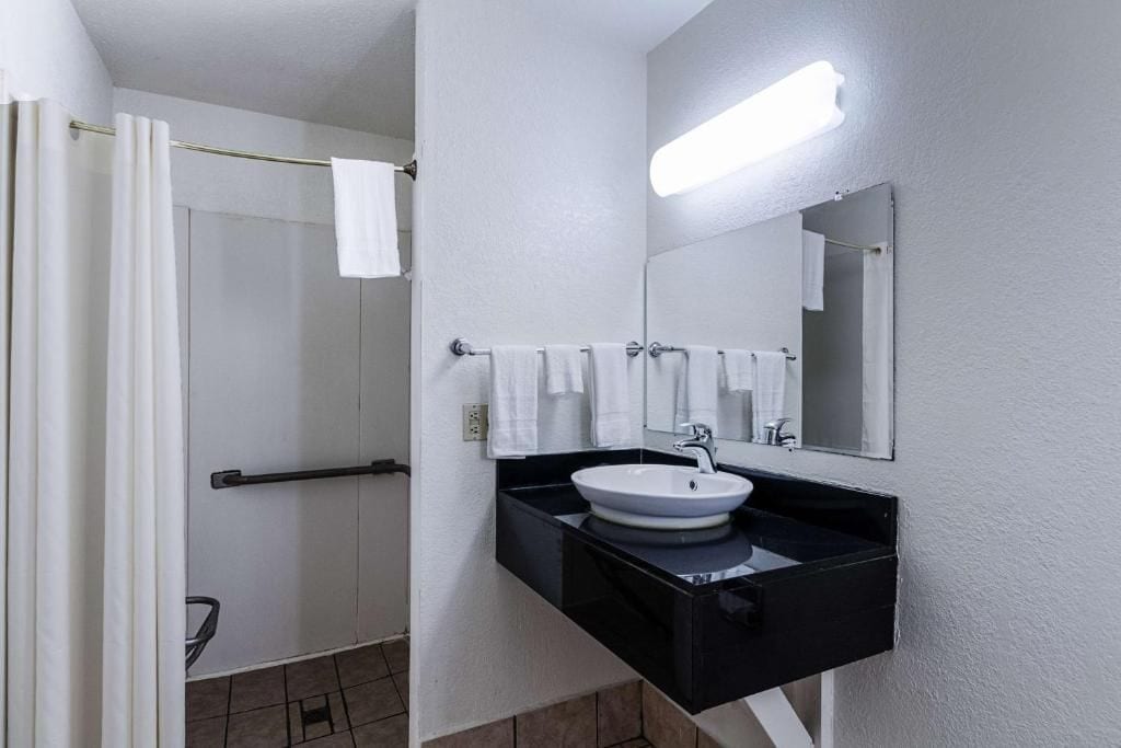 A bathroom with a white sink, black countertop, and a mirror above it. There is a towel rack with white towels and a shower curtain.