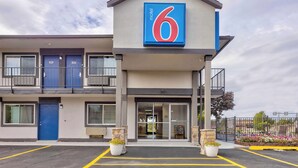 A motel with a prominent '6' sign, a blue door, and a parking lot with potted plants. - Motel 6 Oshkosh, WI (Oshkosh)