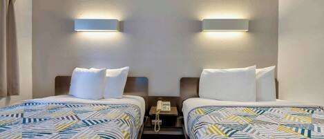 Habitación de hotel con dos camas, una mesita de noche con teléfono e iluminación en la pared.