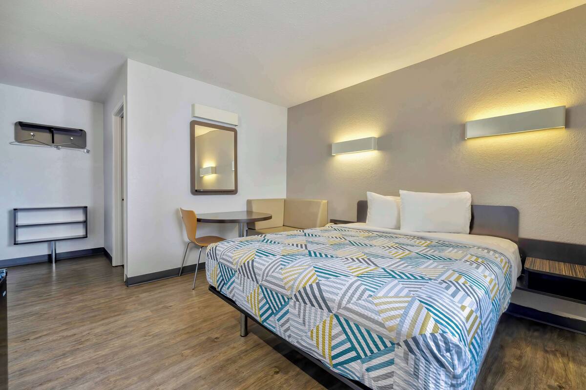 A hotel room with a bed, a desk, a chair, and a small table.