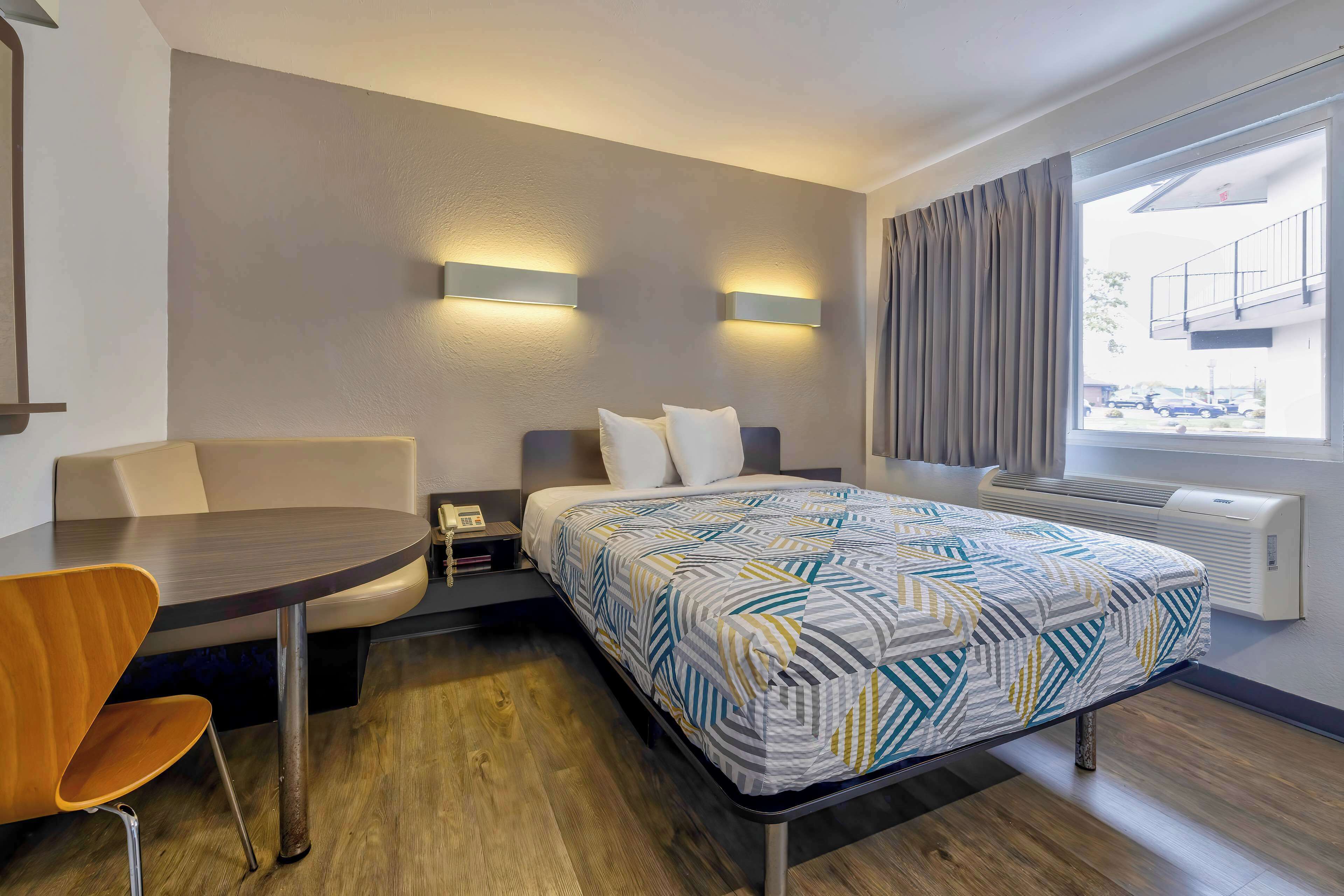 Une chambre d’hôtel comprenant un lit, un bureau avec une chaise, une fenêtre avec des rideaux et un radiateur fixé au mur.