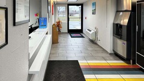 A reception area with a counter, a digital screen, a refrigerator, and a window with a view of the outdoors. - Motel 6 Oshkosh, WI (Oshkosh)