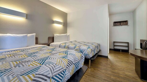 A hotel room with two beds, a bedside table, a desk, and a wall-mounted shelf. - Motel 6 Oshkosh, WI (Oshkosh)
