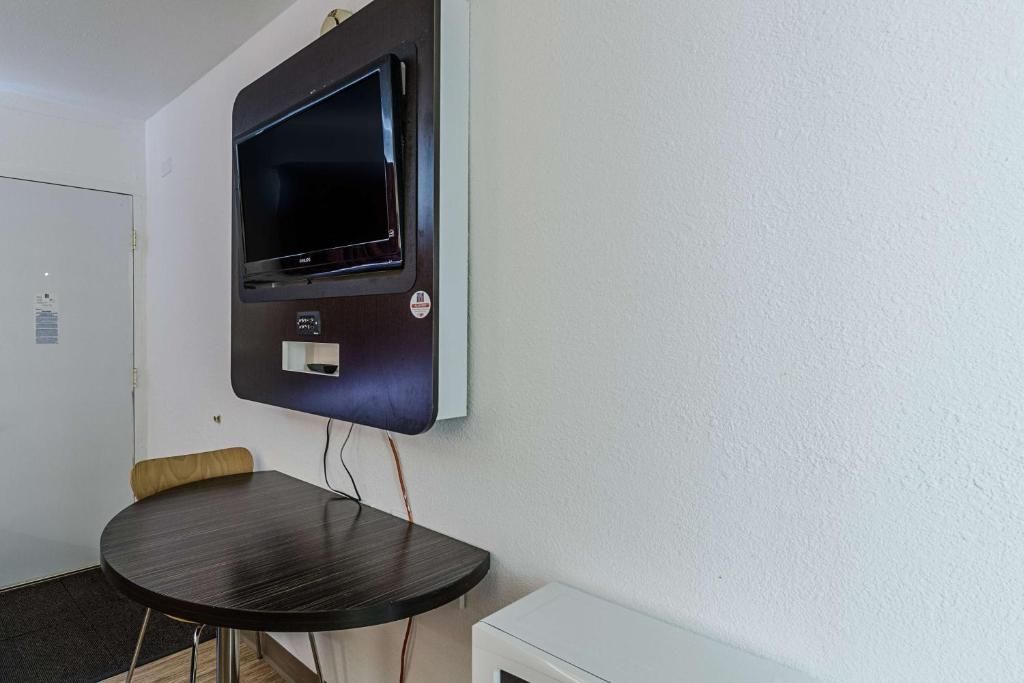 A room with a flat-screen TV mounted on the wall, a round table with a chair, and a white cabinet.