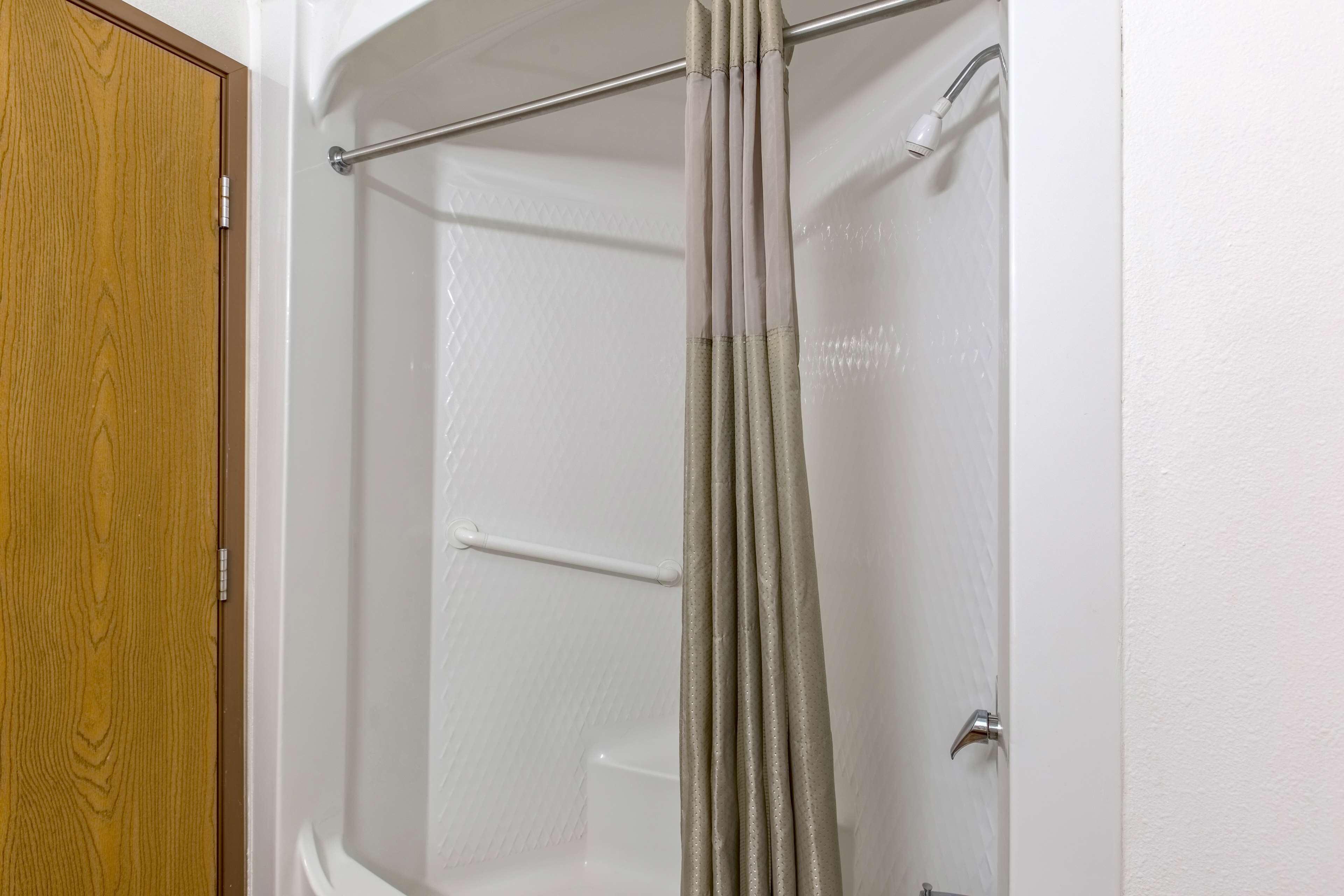 A shower with a beige curtain, a wooden door, and a white tiled wall.