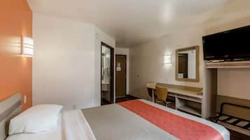A hotel room with a bed, a desk, a chair, a TV, and a mirror.