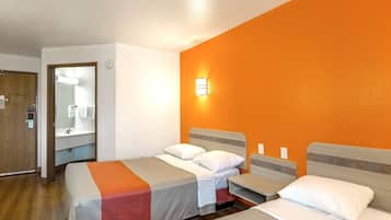 A hotel room with two beds, a bathroom with a mirror and sink, and an orange accent wall.