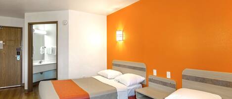 A hotel room with two beds, a bathroom with a mirror and sink, and an orange accent wall.