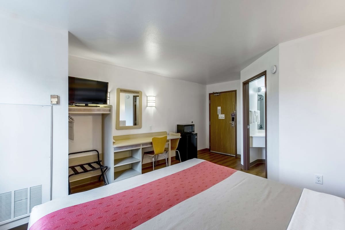 A hotel room with a bed, a desk, a chair, a television, and a wardrobe.