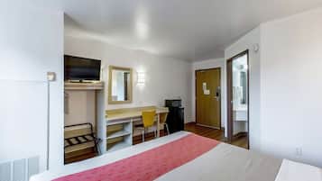 A hotel room with a bed, a desk, a chair, a television, and a wardrobe.