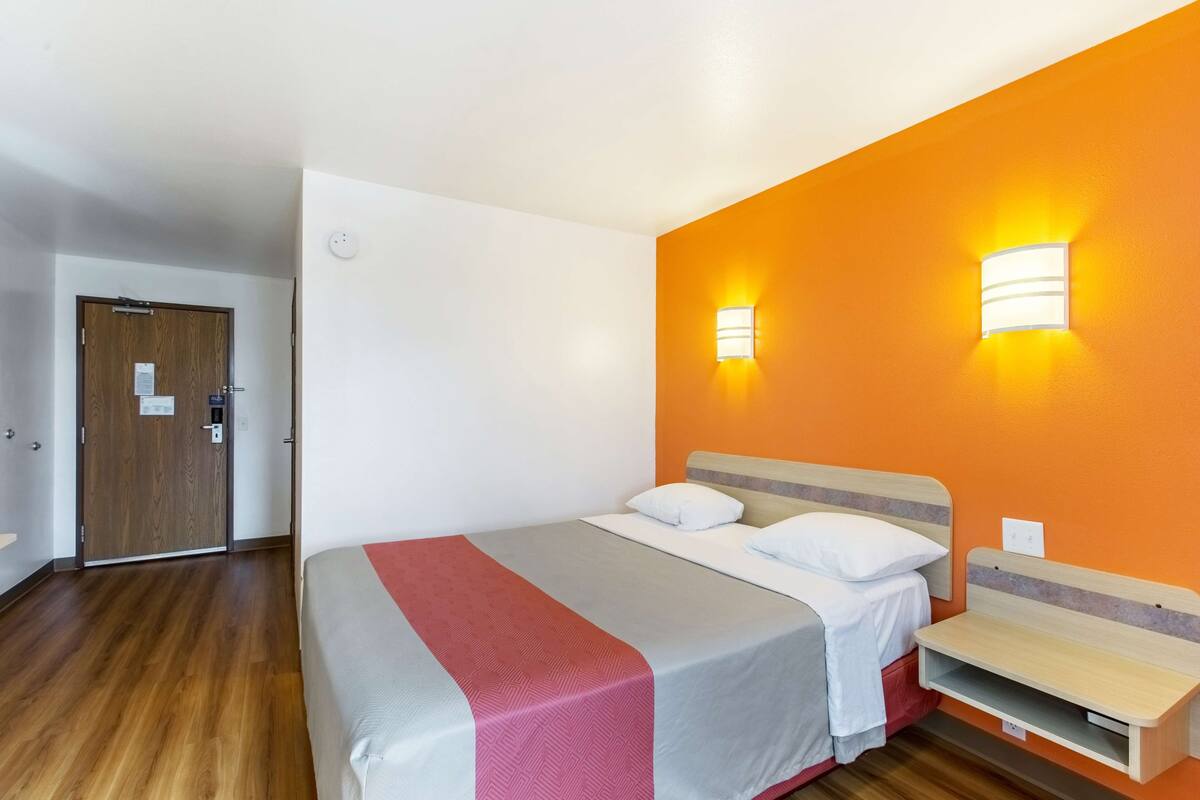 A hotel room with a bed, a bedside table, and two wall-mounted lights.