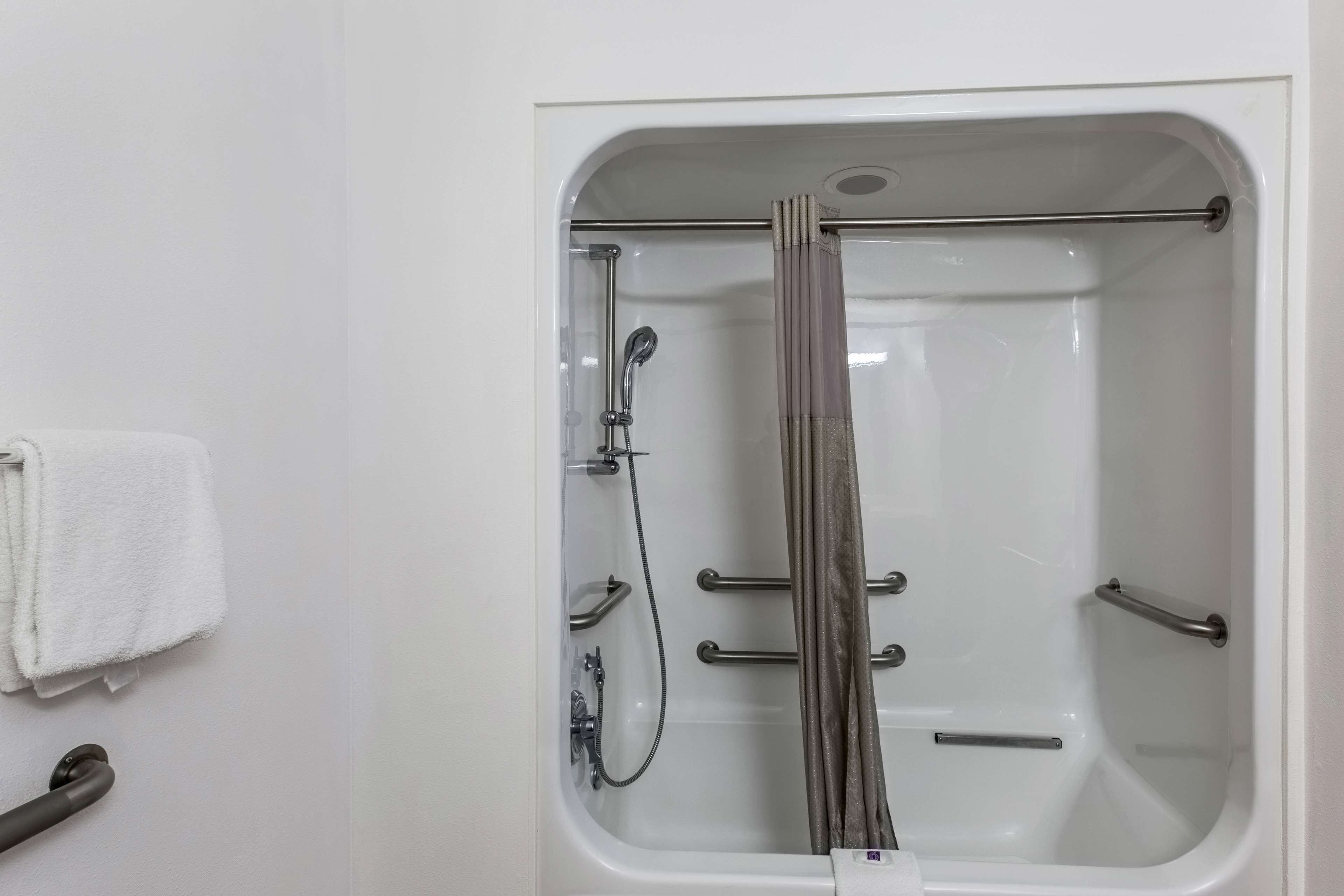 Une baignoire blanche équipée d’une pomme de douche, de barres d’appui et d’un porte-serviettes.