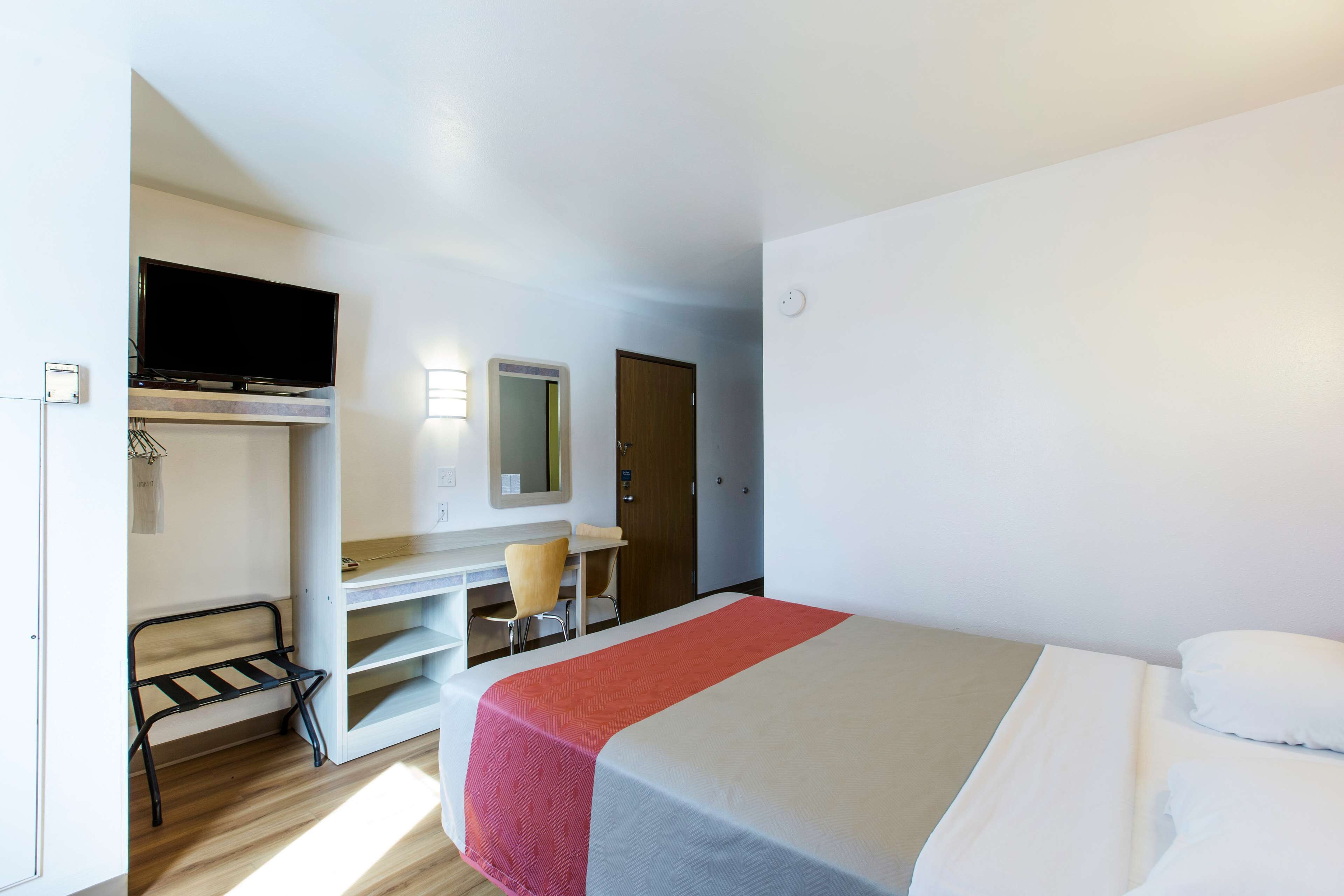 A hotel room with a bed, a desk with a chair, a television, and a wardrobe.