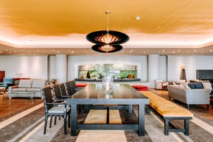 A spacious living room with a large dining table, comfortable seating, a modern chandelier, and a large TV.