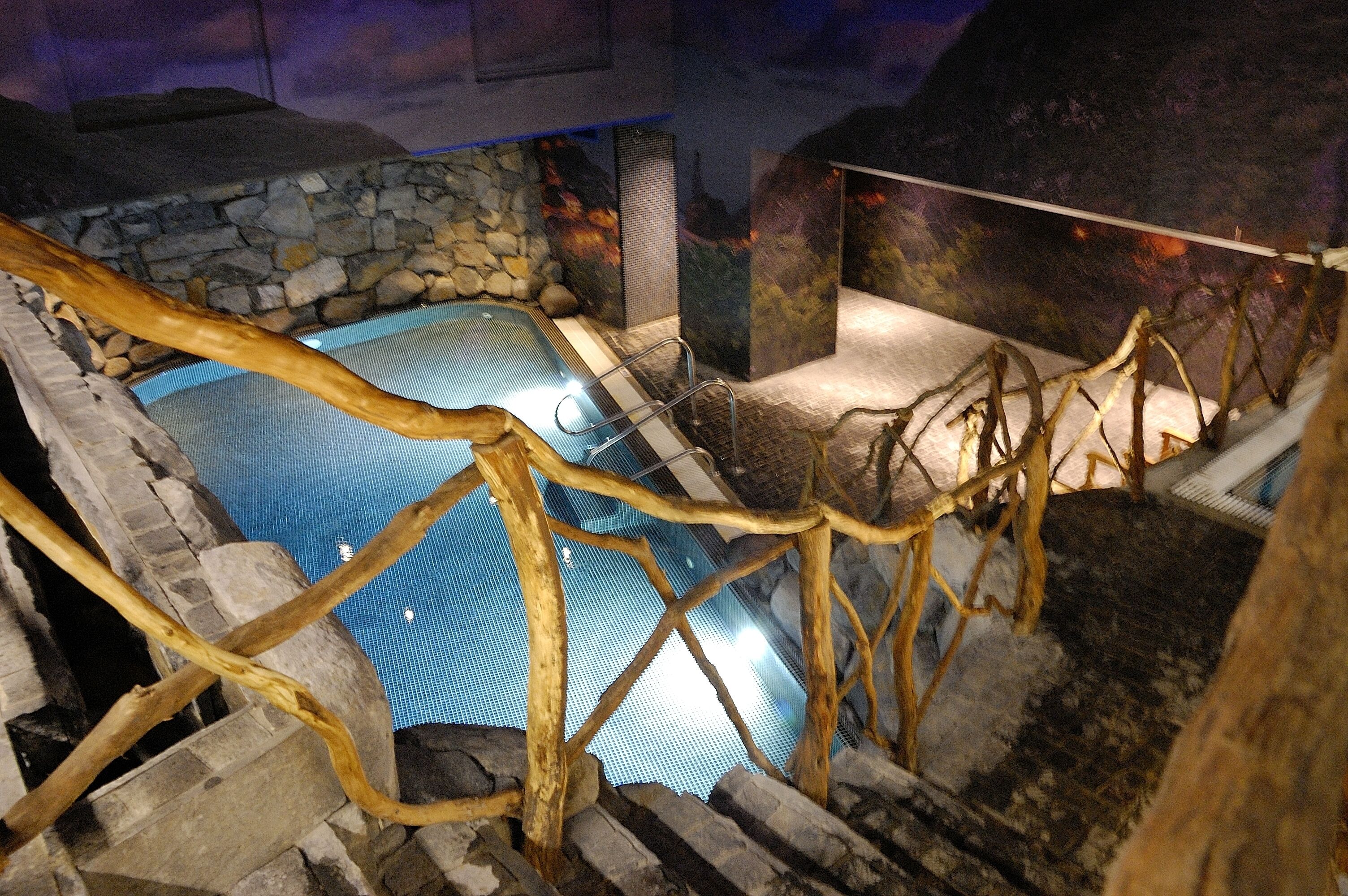 Un espace de détente avec un bain à remous entouré de murs en pierre, agrémenté d’une treille en bois et d’un mur en pierre en arrière-plan.