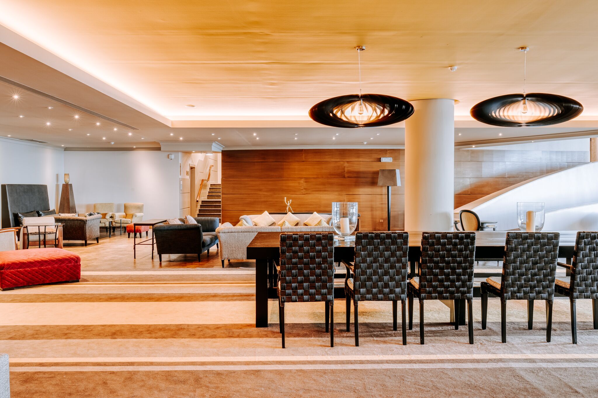 A modern hotel lobby with a dining area featuring a wooden table and black woven chairs.