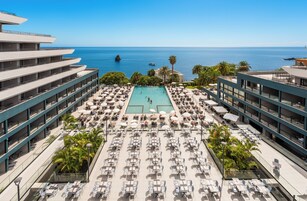 A rooftop pool area with multiple lounge chairs and umbrellas, overlooking a clear blue sea.