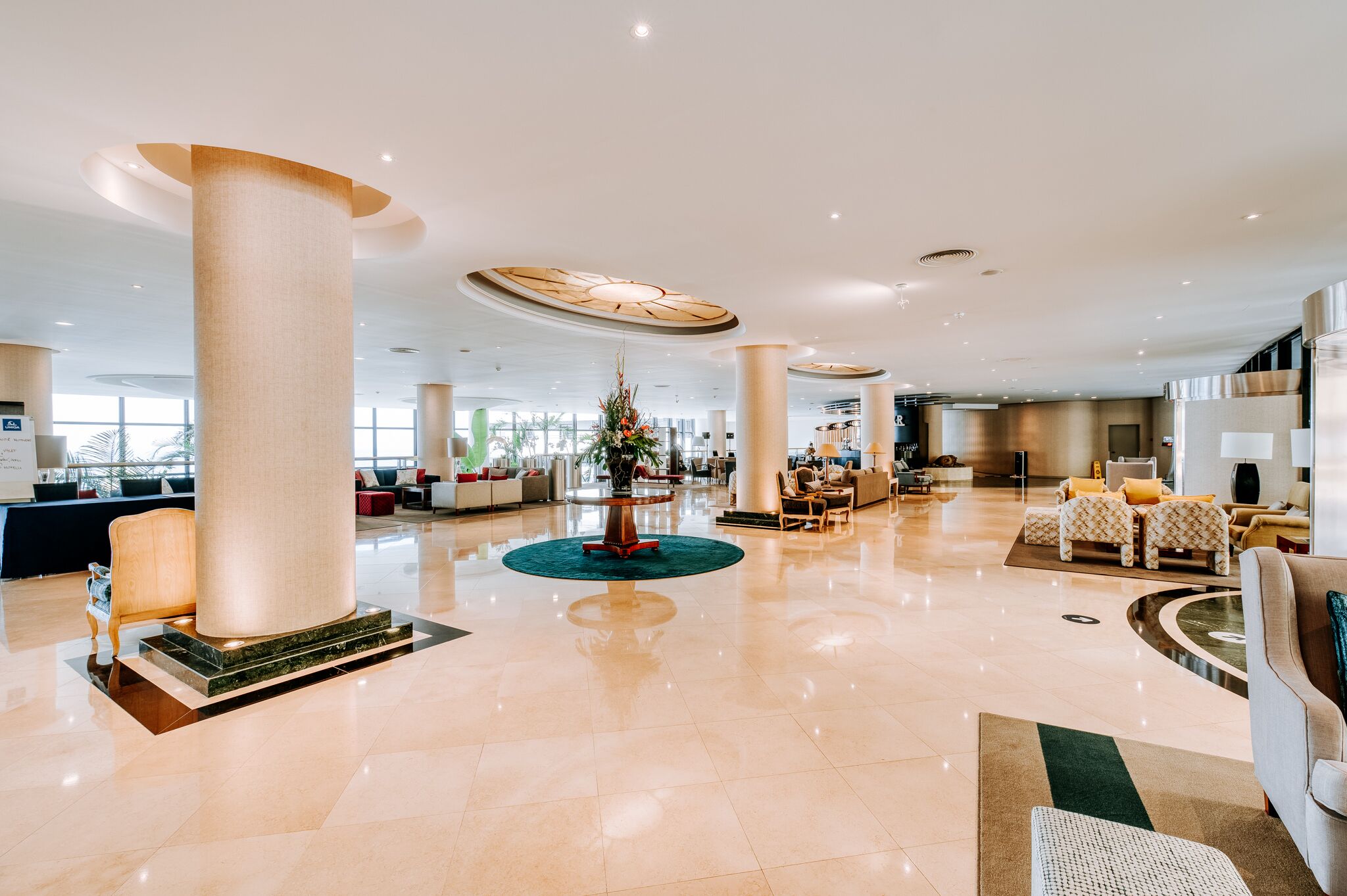 A spacious lobby with high ceilings, large columns, and a central floral arrangement.