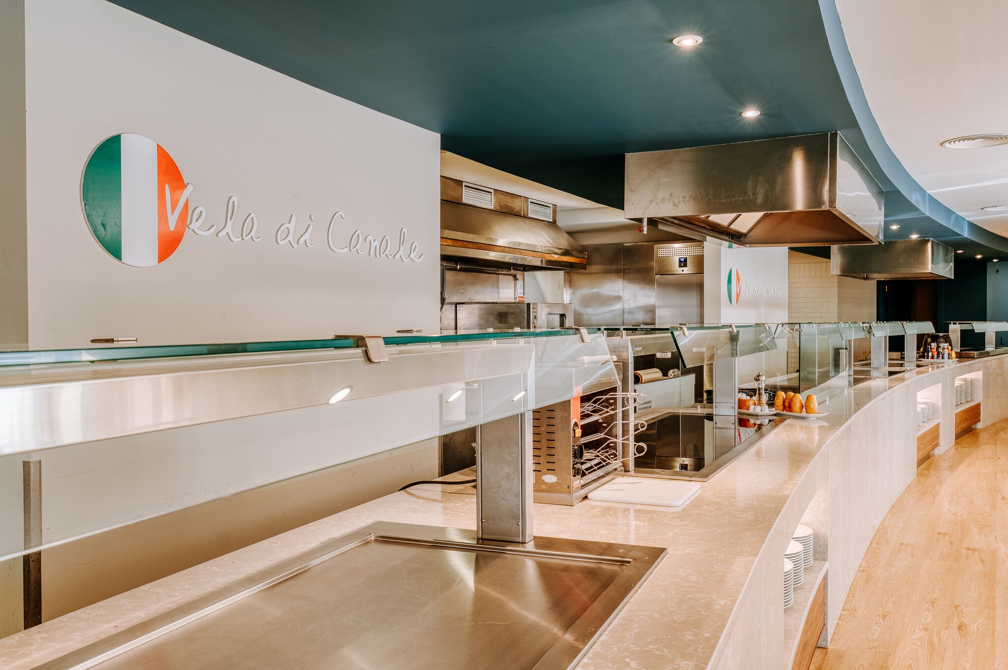 A modern kitchen with stainless steel appliances, a glass counter, and a logo on the wall.