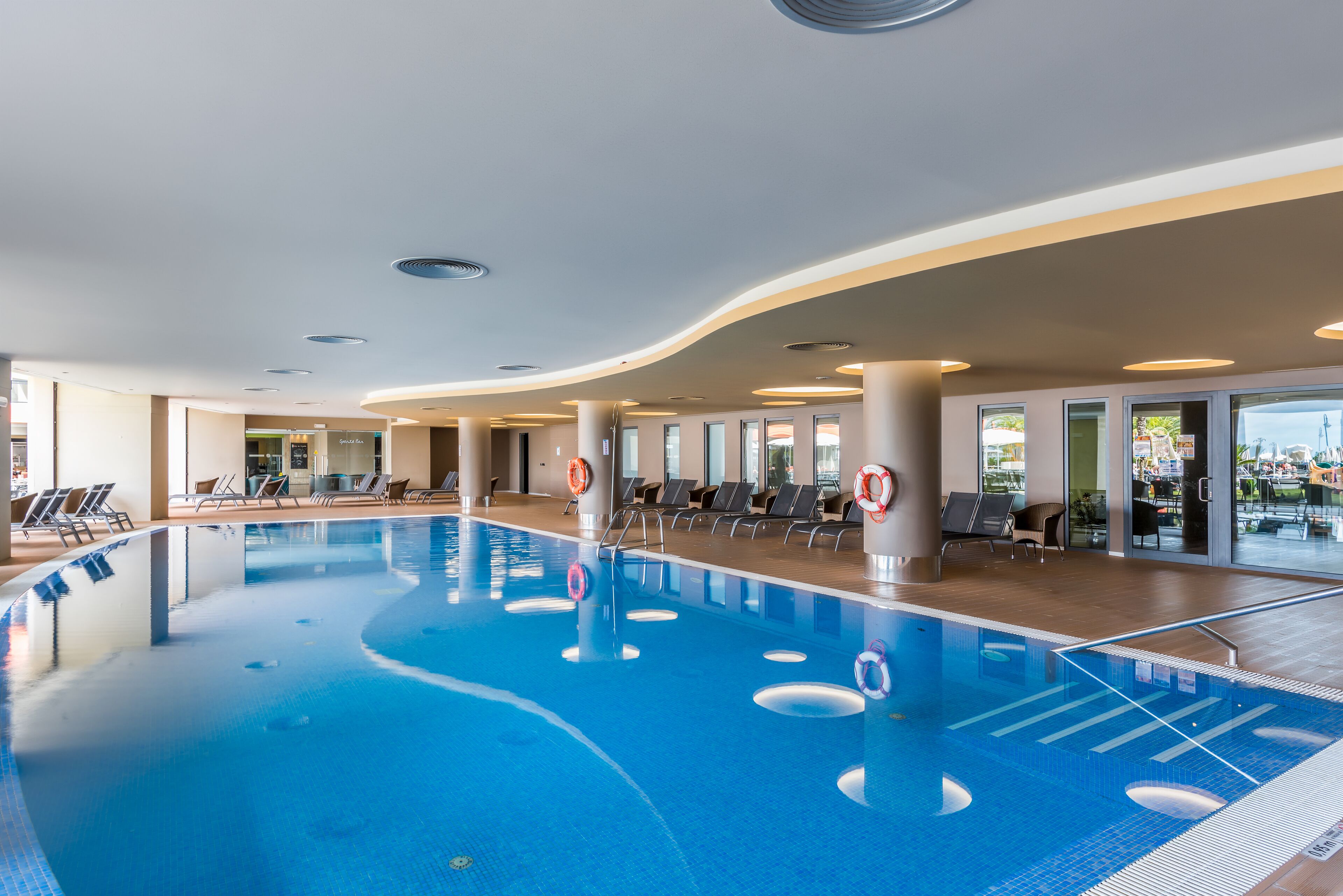 Une piscine intérieure à l’eau claire, entourée de chaises longues et dotée d’un design de plafond moderne.