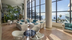 Un espace intérieur vaste et lumineux, aménagé avec des meubles en osier, de grandes fenêtres et offrant une vue sur la mer.
