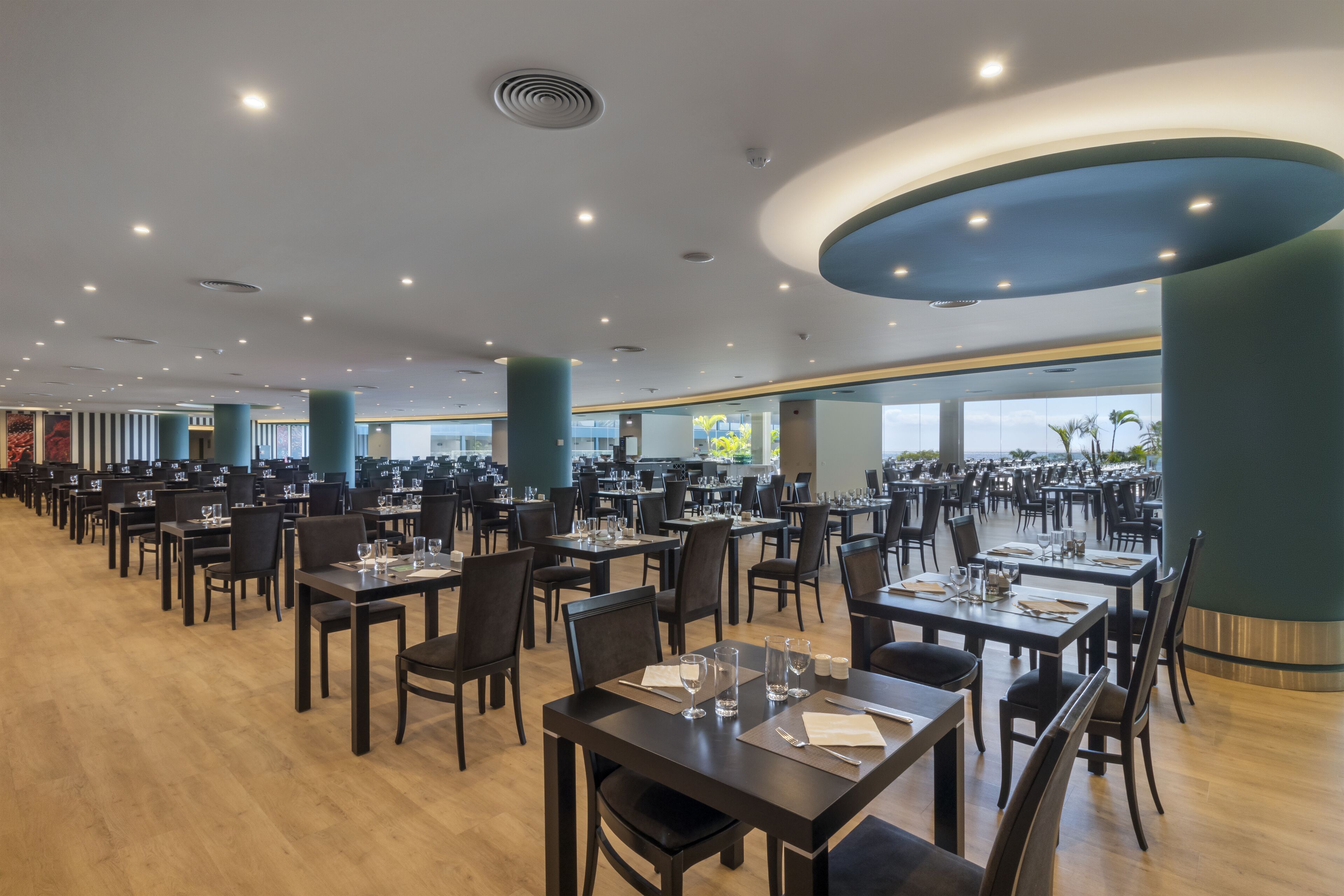 En rummelig restaurant med flere borde og stole, store vinduer og et moderne loftdesign.