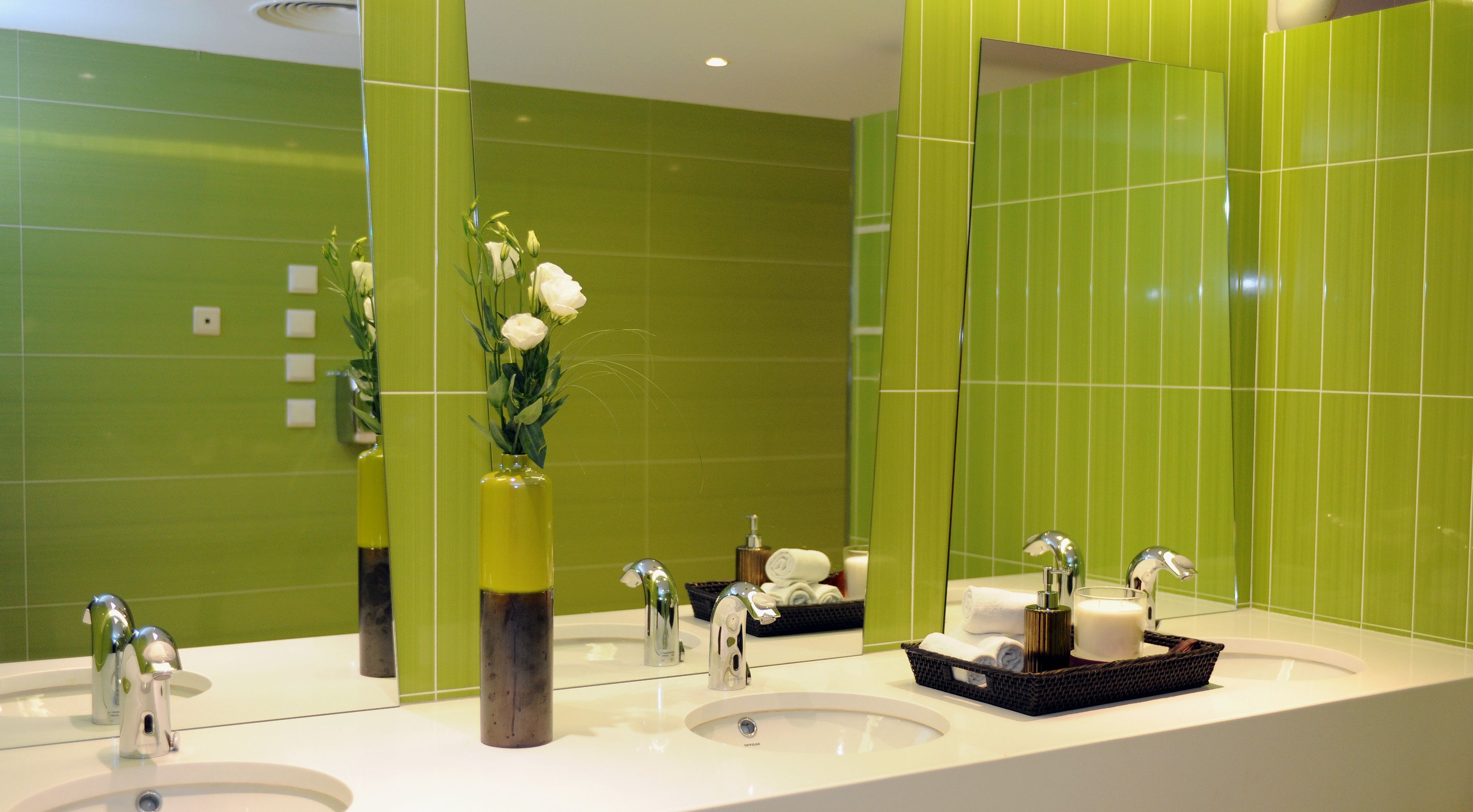 A modern bathroom with green tiles, two sinks, and a mirror reflecting the space.