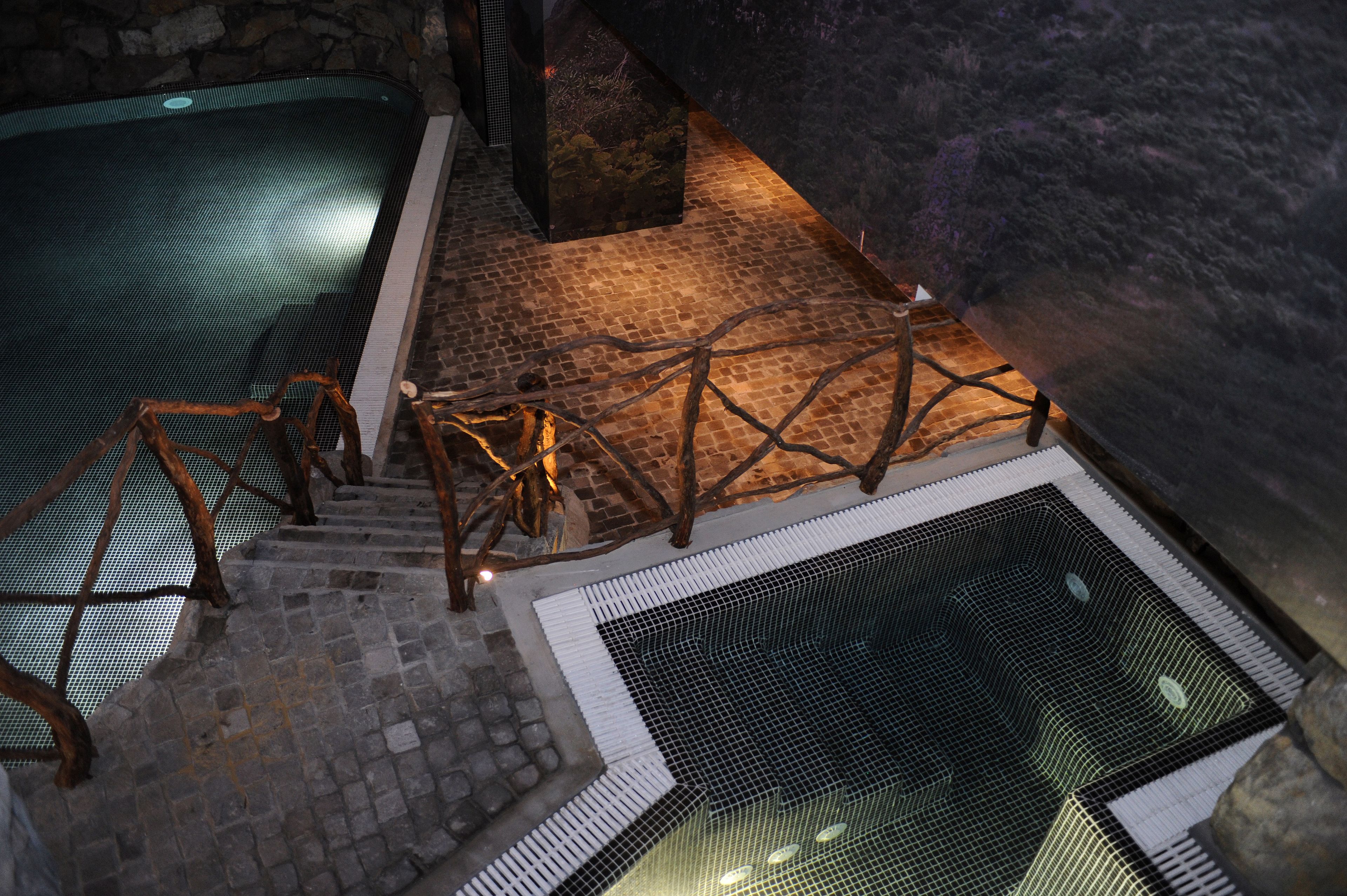 A stone staircase leading to a pool area with a wooden railing and a mesh barrier.