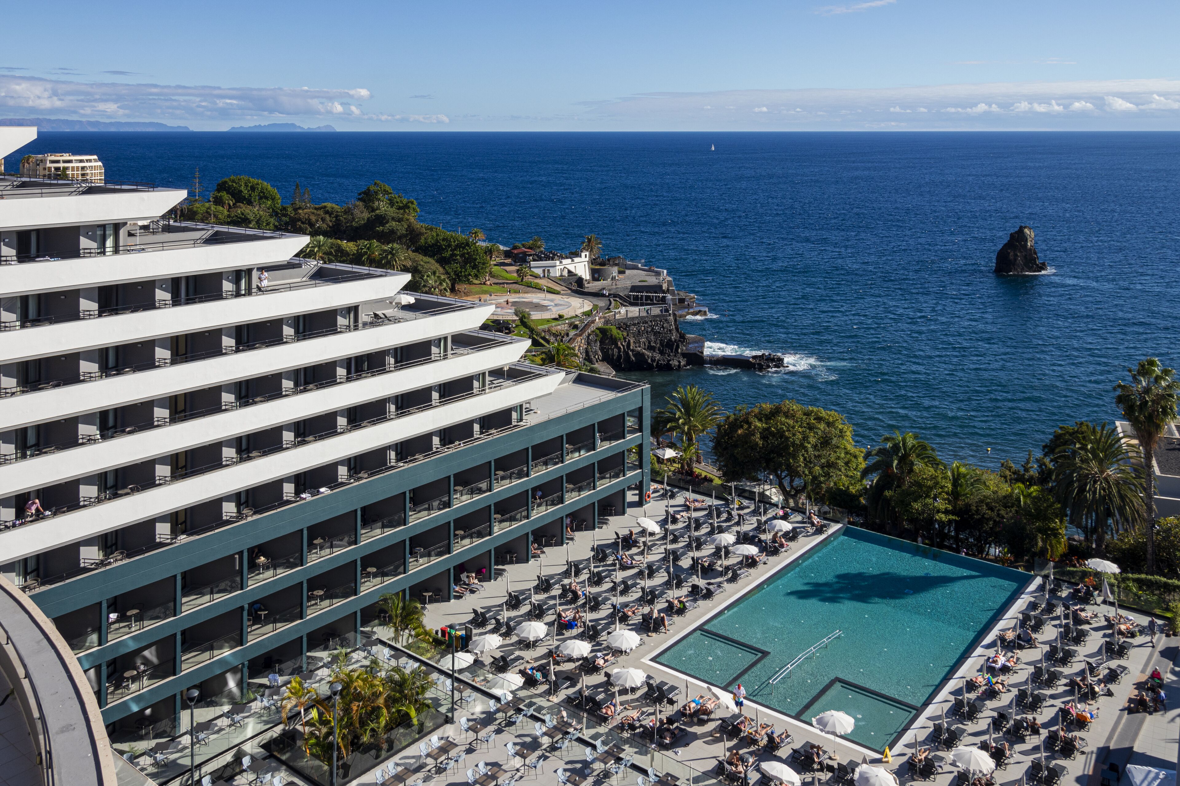 A hotel with a rooftop pool, multiple balconies, and a view of the ocean.