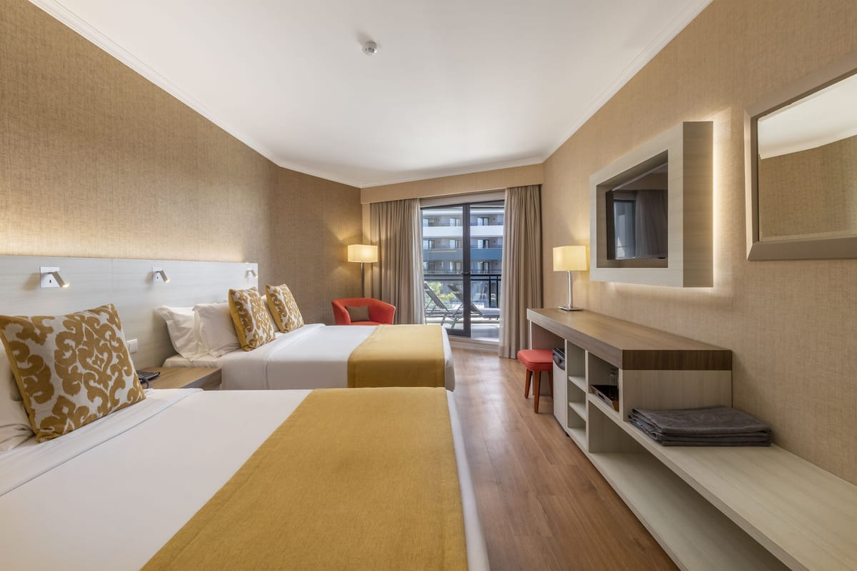 Habitación de hotel con dos camas, un escritorio, una silla, un televisor y un balcón con vistas a edificios.