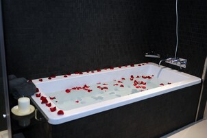 Una bañera llena de agua y pétalos de rosa, una toalla y una botella de loción.