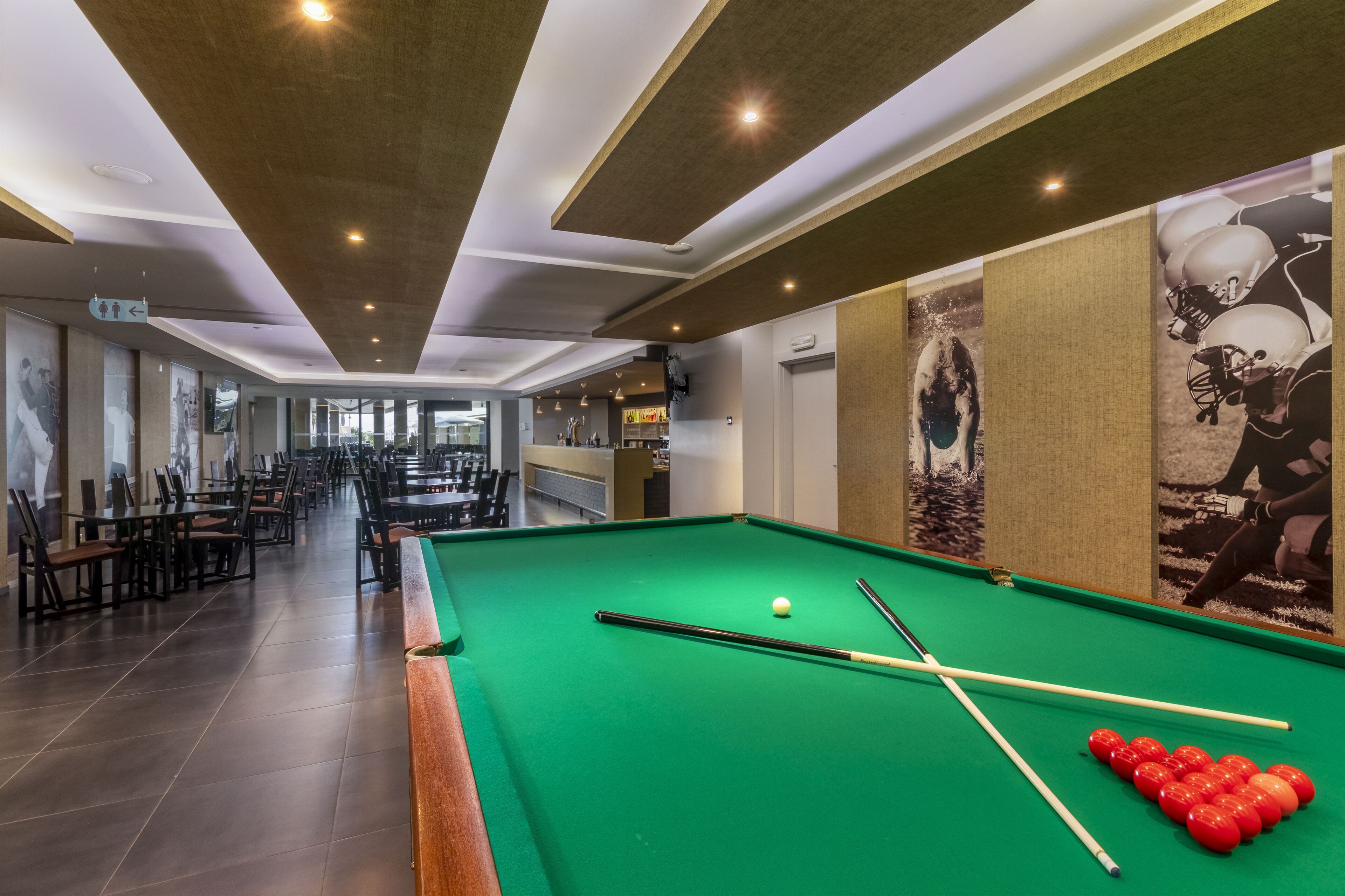 Une table de billard avec des billes et des queues, une table de snooker, et un long couloir avec des tables et des chaises.