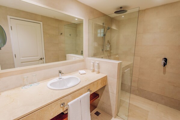 A modern bathroom with a glass-enclosed shower, a large mirror, and a beige countertop with a sink and toiletries.