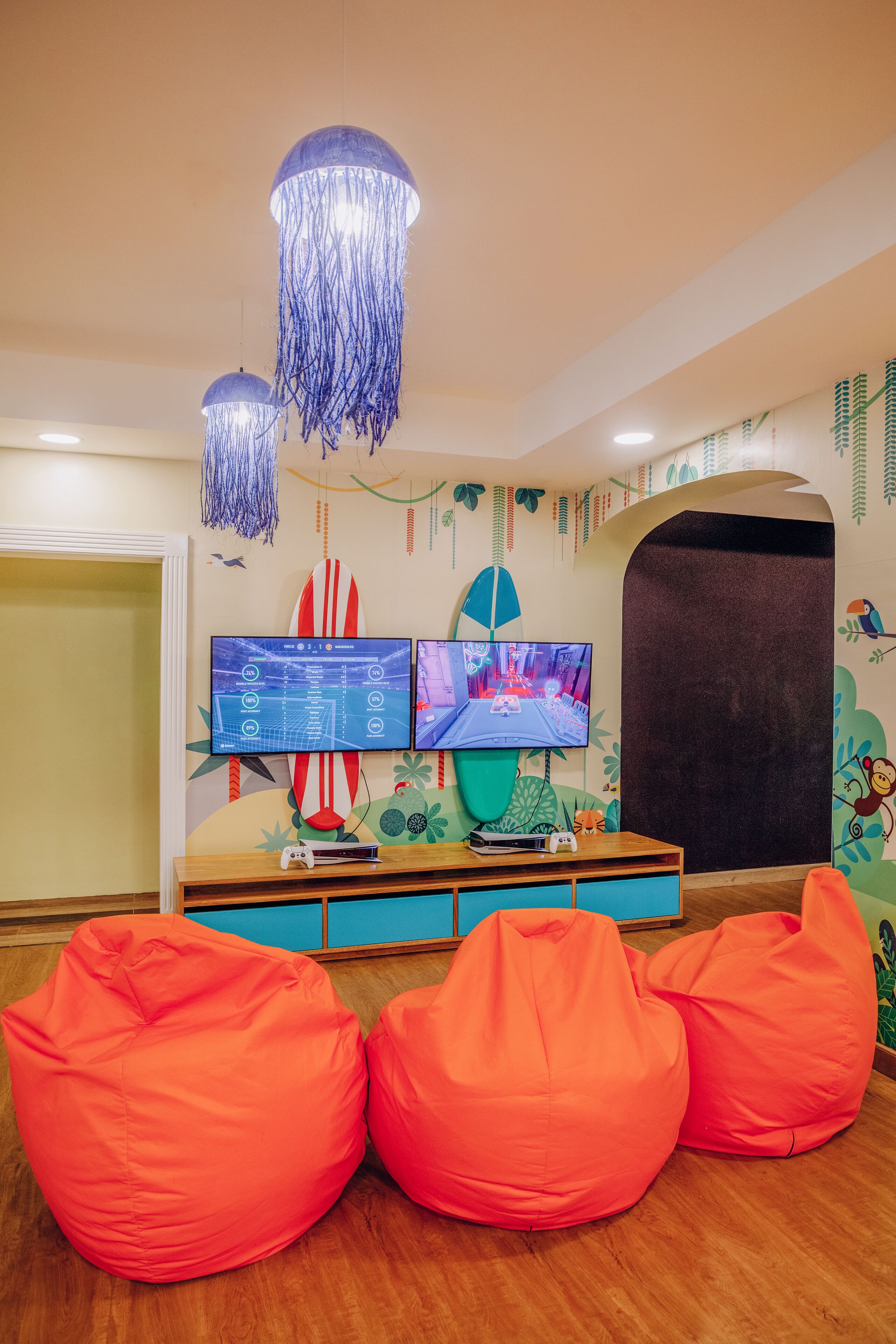 Een kamer met twee monitoren, een surfboard, loungestoelen en een houten vloer.