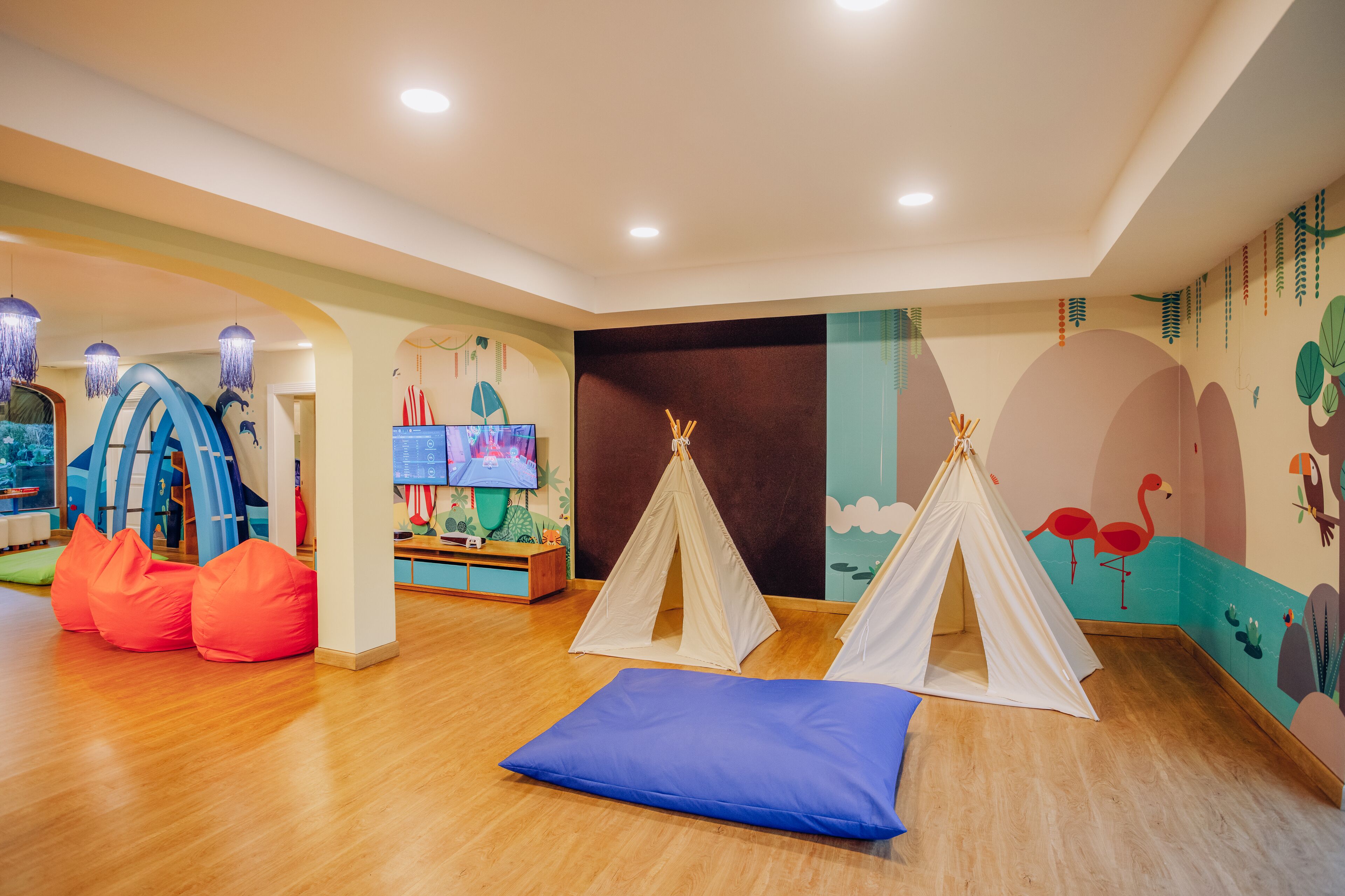 Espaço infantil com tenda de brincar, almofadas de grãos e televisão.