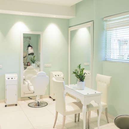 A salon with multiple white chairs, a reception desk, and a large mirror.