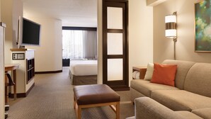 A hotel room with a bed, a TV, a desk, a couch, and a painting on the wall. - Hyatt Place Raleigh-Durham Airport (Morrisville)