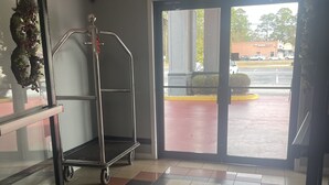 Un hall d’hôtel avec un sol carrelé, un chariot en métal et une grande porte vitrée donnant sur l’extérieur.